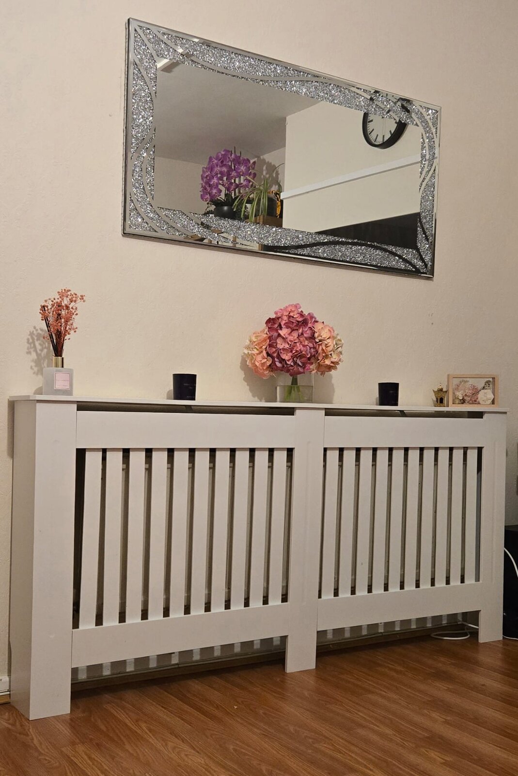White wooden radiator cover assembled in a London hallway, styled with a mirror and flowers